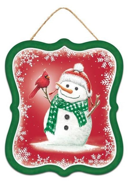 Winter ornament featuring a snowman smiling at a cardinal. This ornament has a green border and a red background. That snowman is wearing a red Santa hat and a green scarf.