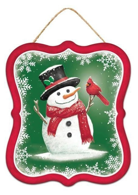 Winter ornament featuring a snowman smiling at a cardinal. This ornament has a red border and a green background. That snowman is wearing a black top hat and a red scarf.