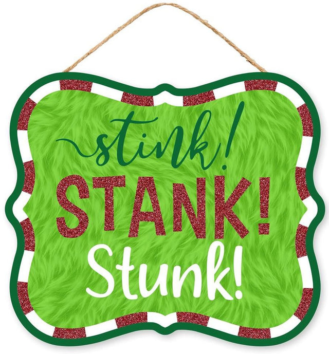 Hanging holiday sign that reads "stink! STANK! Stunk!" in a green, red glitter and white font. The background is designed to look like green fur. There's a red and white border up against a solid green border. Hangs from a jute rope.