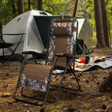 Folding recliner chair with a headrest. There are different color options. This image shows a black frame chair with camouflage sling fabric. It's sitting in a campsite in the middle of the woods.