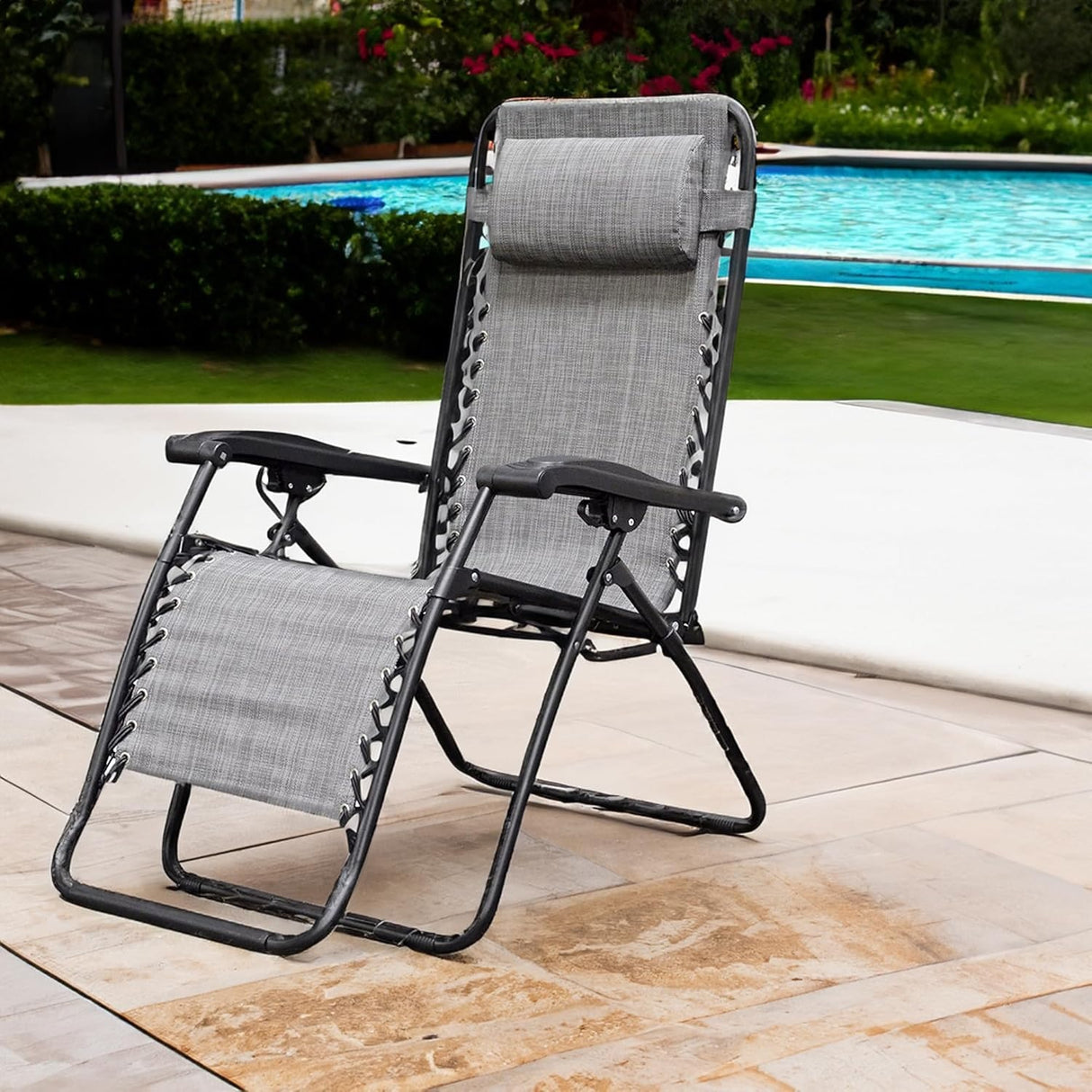 Folding recliner chair with a headrest. There are different color options. This image shows a black frame chair with grey sling fabric. It's sitting on a stone patio next to an inground pool.