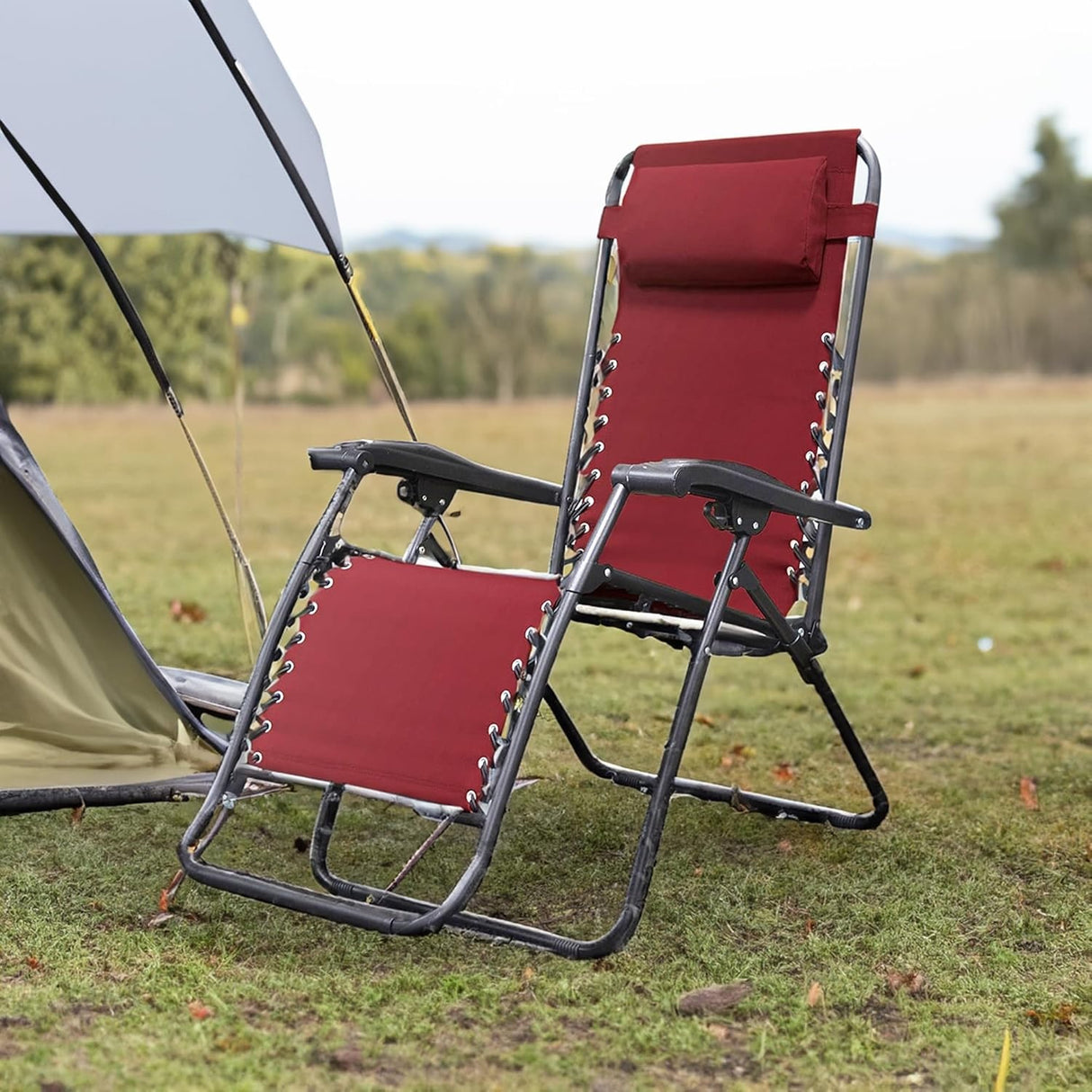 Folding recliner chair with a headrest. There are different color options. This image shows a black frame chair with burgundy sling fabric. It's sitting on the grass next to a tent.