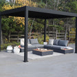 This is a lifestyle image showing the Georgetown sun shelter. The frame is a Charcoal gray color. Underneath the sun shelter, there are two outdoor loveseats with a table in the center.