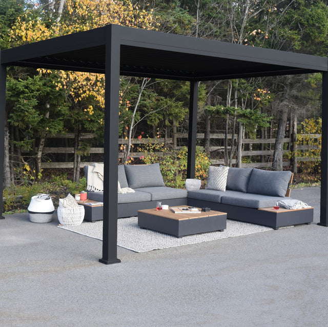 This is a lifestyle image showing the Georgetown sun shelter. The frame is a Charcoal gray color. Underneath the sun shelter, there are two outdoor loveseats with a table in the center.