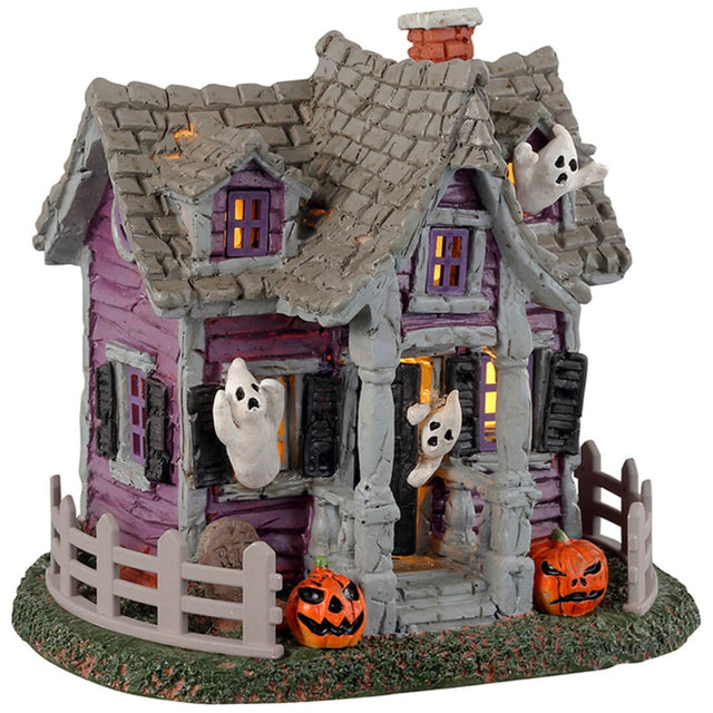 Resin village accent for a Lemax display. Designed to look like a purple, rundown house with ghosts coming out of the windows. There are jack-o-lanterns on either side of the porch and a gray fence around the house.