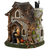 Resin table accent for a Lemax display. Designed to look like an old, stone cottage with vines growing on it. There are also trees growing into the cabin. There's a witch sweeping the front porch and a black cat standing on top of the chimney.