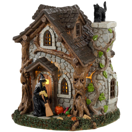 Resin table accent for a Lemax display. Designed to look like an old, stone cottage with vines growing on it. There are also trees growing into the cabin. There's a witch sweeping the front porch and a black cat standing on top of the chimney.