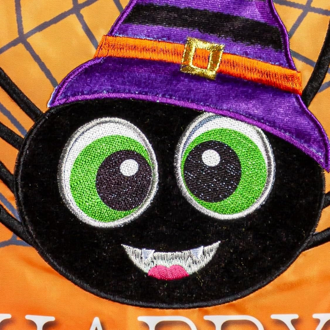 Outdoor Halloween flag. The background is orange and has a gray spiderweb. There are three large, smiling spiders and a message that reads "HAPPY HALLOWEEN." The spiders are all wearing colorful hats. One is pink, one is lime green and one is purple.