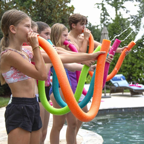 This is a lifestyle image showing five kids using different colored pool noodles as water guns. The pool noodles get filled with water and then you blow air through one side of the noodle and the water comes out the other side.