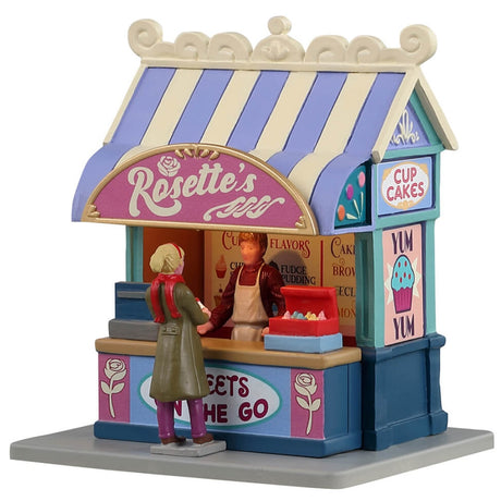 Resin village accent for a Lemax display. Designed to look like a cupcake vendor booth. It's run by Rosette and it's sweets to go. The colors of the booth are light purple, tan, pink, light blue and dark blue.