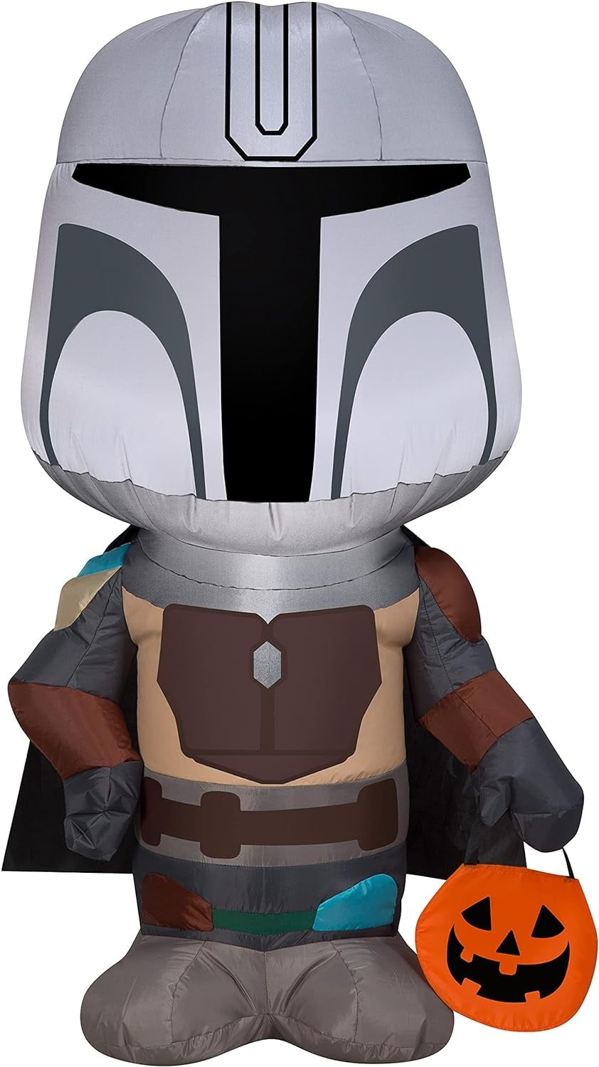 Halloween inflatable shaped like The Mandalorian from the Star Wars universe. He's holding a treat tote bag that looks like a carved pumpkin.
