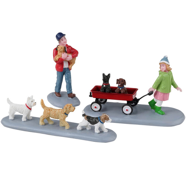 Resin figurines for a Lemax display. Designed to look like puppies on parade. There's a boy carrying a puppy and a young girl pulling a red wagon with two dogs inside. There are three other dogs following them.