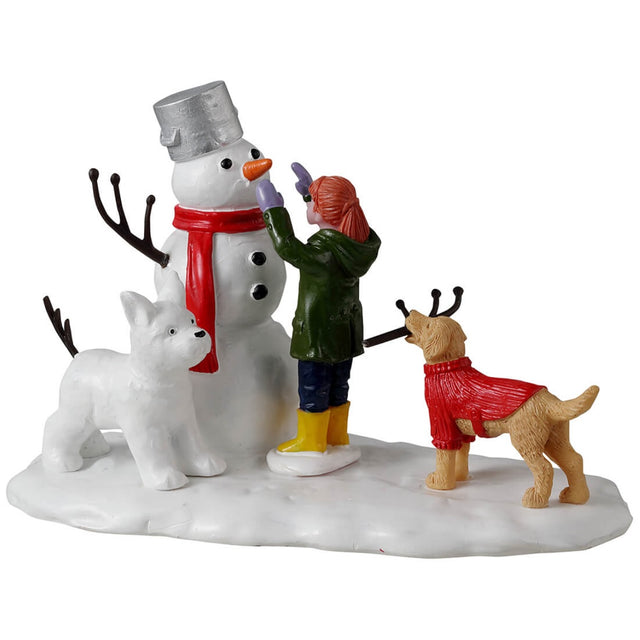 Resin village accent for a Lemax display. Designed to look like a young girl putting the finishing touches on a snowman. There's a dog holding a twig, trying to help. There's a dog made out of snow standing next to the snowman.
