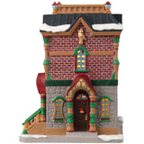 Porcelain lighted building for a Lemax display. Designed to look like a brick building decorated for Christmas with wreaths and garlands. There's snow on the roof and on the sidewalk. 