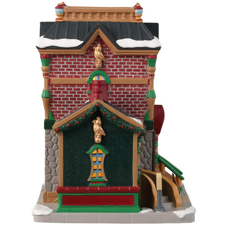 Porcelain lighted building for a Lemax display. Designed to look like a brick building decorated for Christmas with wreaths and garlands. There's snow on the roof and on the sidewalk. 