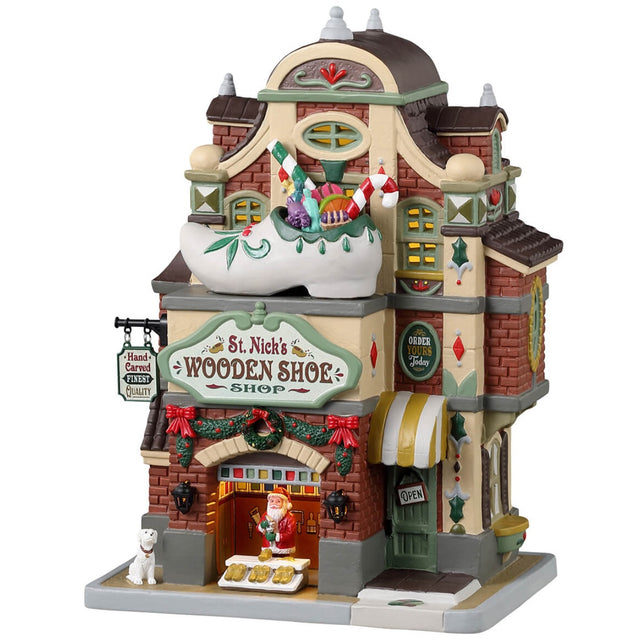 Porcelain lighted building for a Lemax display. Designed to look like a brick shoe store. There's a large wooden shoe statue with gifts inside on the roof. Santa is near the front, offering to help you find the perfect shoes. There's also a white dog on the sidewalk.