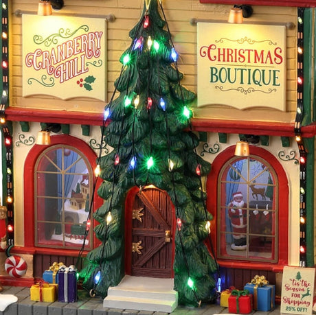 Resin lighted building for a Lemax display. Designed to look like a Christmas store. There are decorative ornaments on the roof, a large decorated Christmas tree over the front door, a nutcracker, presents and a snowman on the sidewalk.