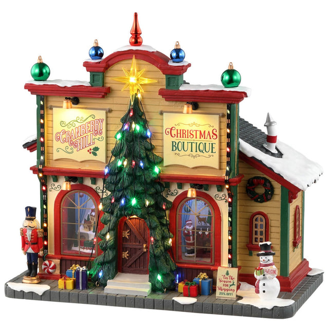 Resin lighted building for a Lemax display. Designed to look like a Christmas store. There are decorative ornaments on the roof, a large decorated Christmas tree over the front door, a nutcracker, presents and a snowman on the sidewalk.