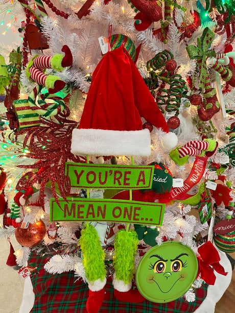 Hanging decoration for Christmas. The top is a red Santa hat with a white cuff and a white ball at the tip of the hat. Underneath that is a sign that reads "YOU'RE A MEAN ONE" and the text is colored with red glitter. Under that are two green furry legs with red elf shoes.