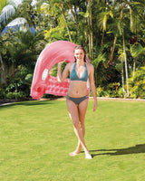 This is a lifestyle image showing a woman holding the pink pool lounge chair over her shoulder. There are lots of palm trees in the background.
