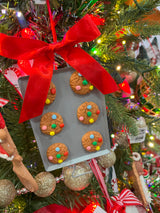 Ornaments shaped like cookies with M&M candies on them, resting on silver trays.