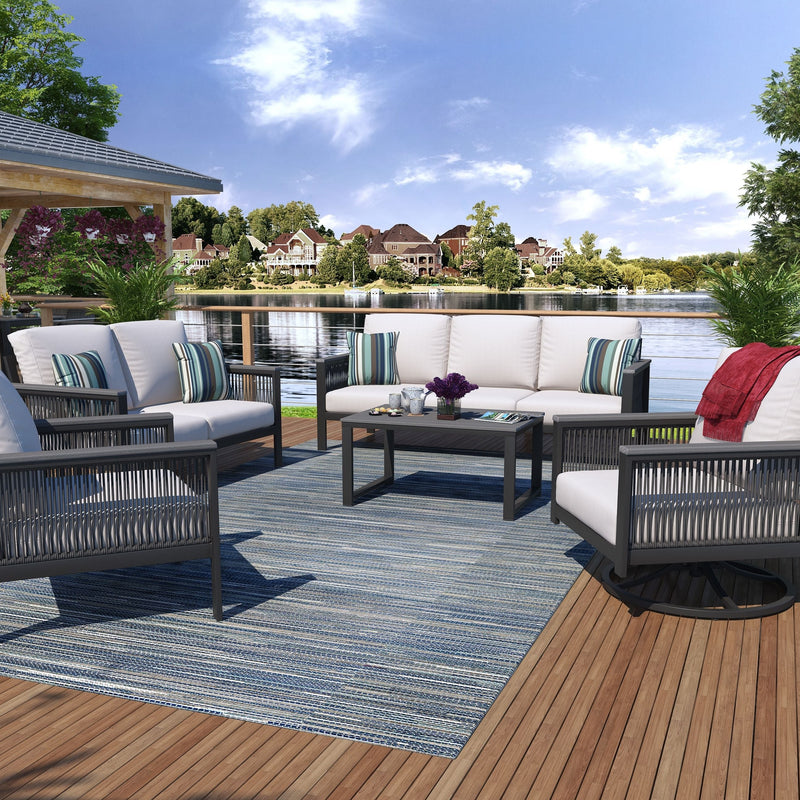 Outdoor furniture set arranged on a deck with a view of a body of water and trees in the background, including a sofa, loveseat, club chairs, and an end table.