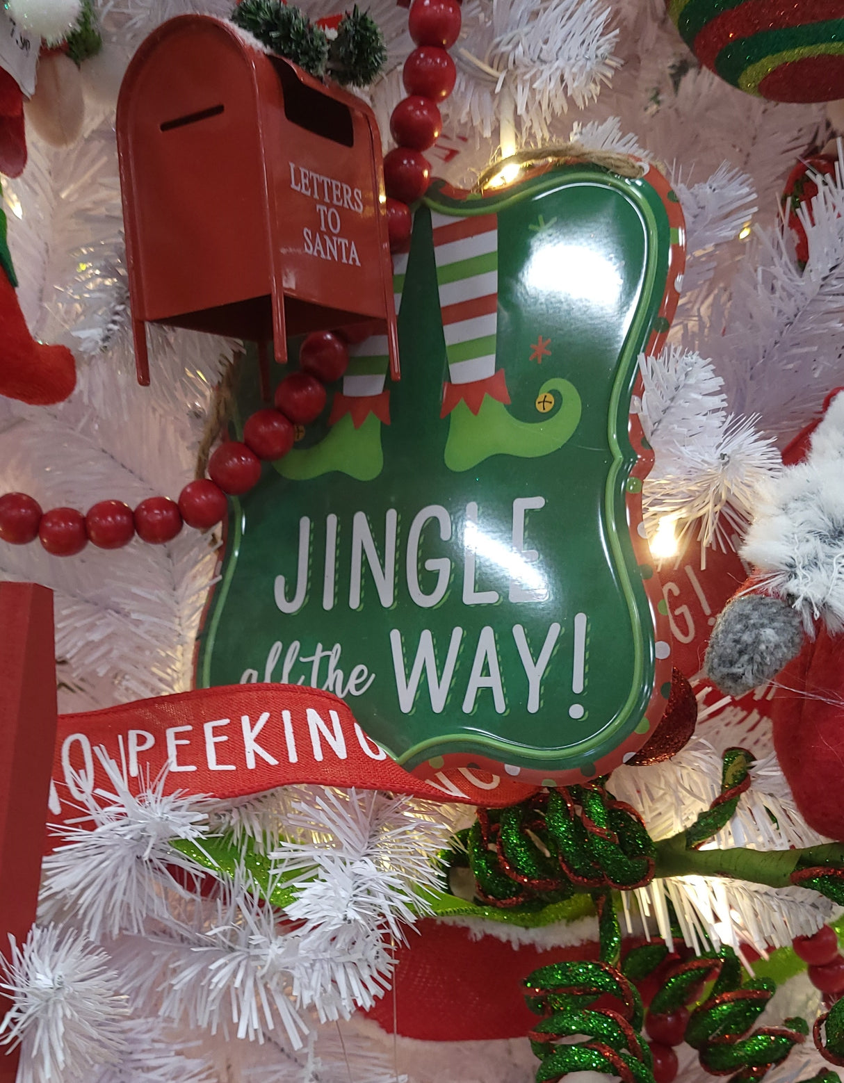 Christmas sign hanging from a jute rope on a Christmas tree with other ornaments and tinsel.