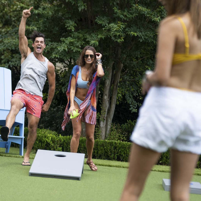 This is a lifestyle image for the cornhole set from Ledge Lounger. This picture shows a man and woman cheering, seemingly because they just scored some points.