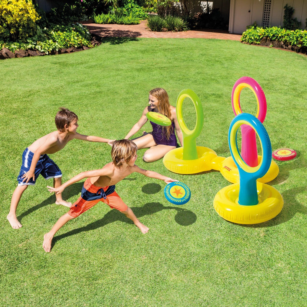 This is a lifestyle image showing two young boys throwing discs through inflatable rings. The rings are set up in the grass. 