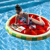 This is a lifestyle image showing a woman resting on this inflatable watermelon float while she reads a magazine.