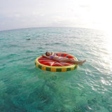 This is a lifestyle image showing a woman laying on the watermelon float while floating in the ocean.
