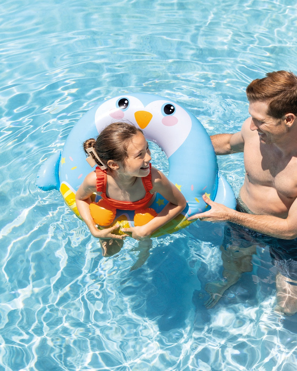 This is a lifestyle image showing a little girl inside the penguin inner tube while her dad looks on.