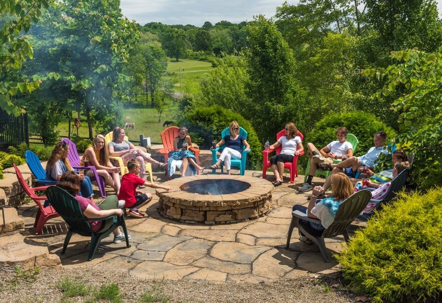 A bunch of different colored Adirondack chairs with people sitting on them around a fire.
