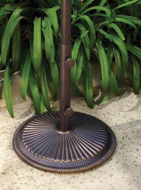This image shows a bronze colored umbrella base on the floor next to a plant.