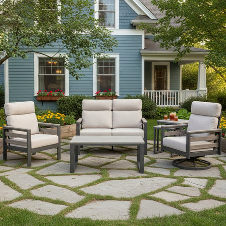 This is a lifestyle image showing this cushioned patio furniture set on a stone patio on a stone patio in the backyard of a light blue house.