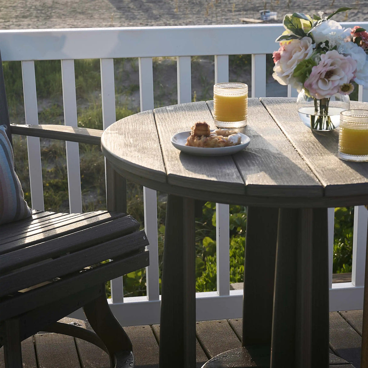 This is a lifestyle image showing the Black colored Balcony Table next to a matching chair on a wooden balcony in a backyard.