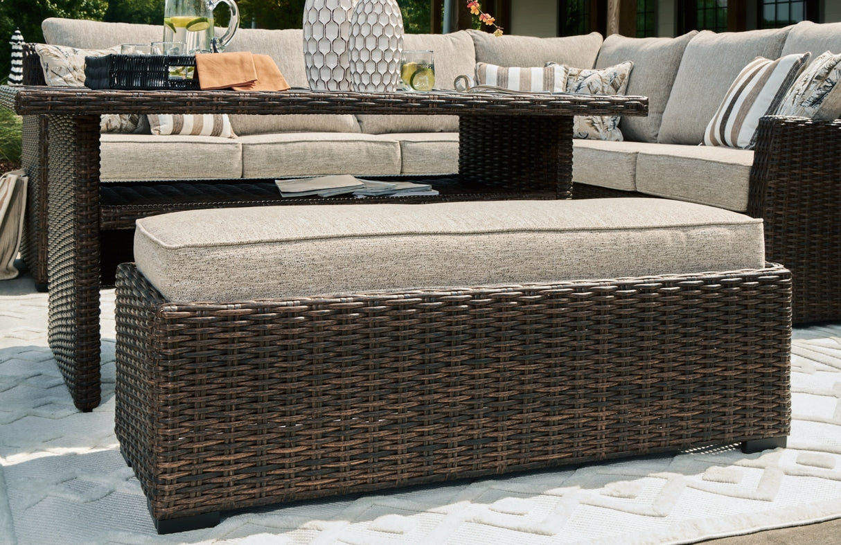 This is an up close view of the cushioned bench. The frame is a brown wicker and the cushion is beige.