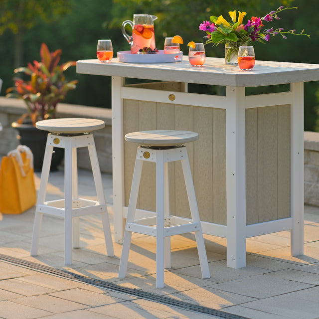 This is a lifestyle image showing a Birch and White serving bar with two matching bar stools in front of it. They're all on a stone patio. On top of the serving bar, there are glasses of strawberry lemonade and a vase full of colorful flowers.