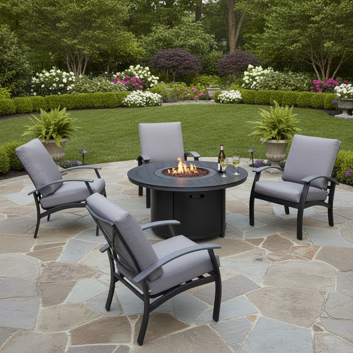 This is a lifestyle image showing four cushioned patio chairs around a circular fire pit table on a stone patio in a grassy backyard.