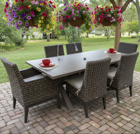This is a lifestyle image showing this wicker patio dining set on a brick patio. There are hanging pots of flowers above the table.