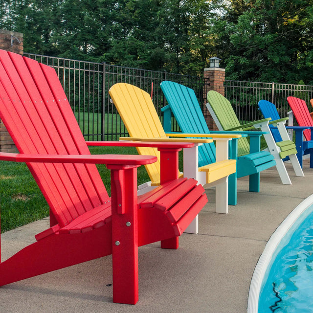 This is a lifestyle image showing six Adirondack chairs on the concrete next to a pool. The chairs are all different colors. The chairs are Red, Yellow & White, Aruba Blue, Lime Green & White, Blue and Red & White.