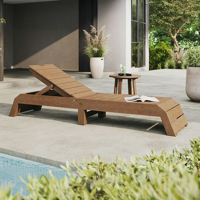This is a lifestyle image showing the Antique Mahogany colored chaise lounge chair on a concrete patio next to a pool.
