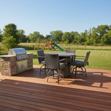 This is a lifestyle image showing the patio furniture set on a wooden porch in a grassy backyard. The porch also has a grill on it and in the back of the yard, there's a playset.