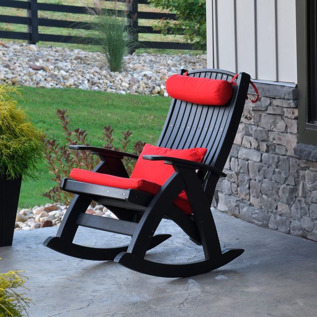 This is a lifestyle image showing a Black colored rocking chair on a concrete patio on the side of a house. There are red cushions on the chair (those are sold separately).