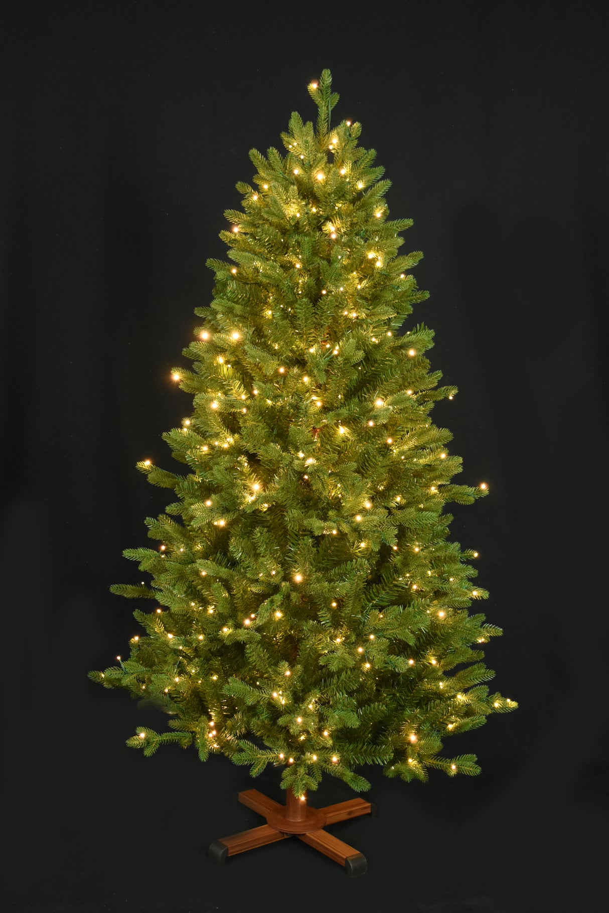 This image shows the tree pre-lit with Warm White Starry Lights. It has a wooden tree stand. This shows the tree on a black background.