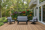 This is a lifestyle image showing this patio furniture set on a wooden deck. There's a black trellis on the deck decorated with lots of colorful flowers.