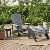 This is a lifestyle image showing the black and gray colored Adirondack chair with a matching end table and ottoman. The furniture is on a wooden deck with a circular, jute rug. The deck is surrounded by lots of foliage and potted cacti.