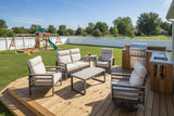 This is a lifestyle image showing this cushioned patio furniture set on wooden deck in a grassy backyard. In the distance, there's a wooden playset. On the deck behind the furniture is a built-in grill.
