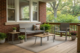 This is a lifestyle image showing this patio furniture set on a wooden back porch beside a brick house. There are lots of potted plants and a fun throw pillow on the loveseat.