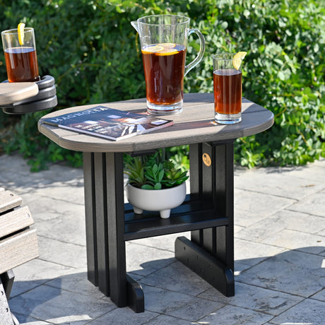 This is a lifestyle image showing the Coastal Gray and Black colored end table. There's a magazine and a pitcher of iced tea on top of the table. And on the shelf underneath the table, there's a succulent plant.